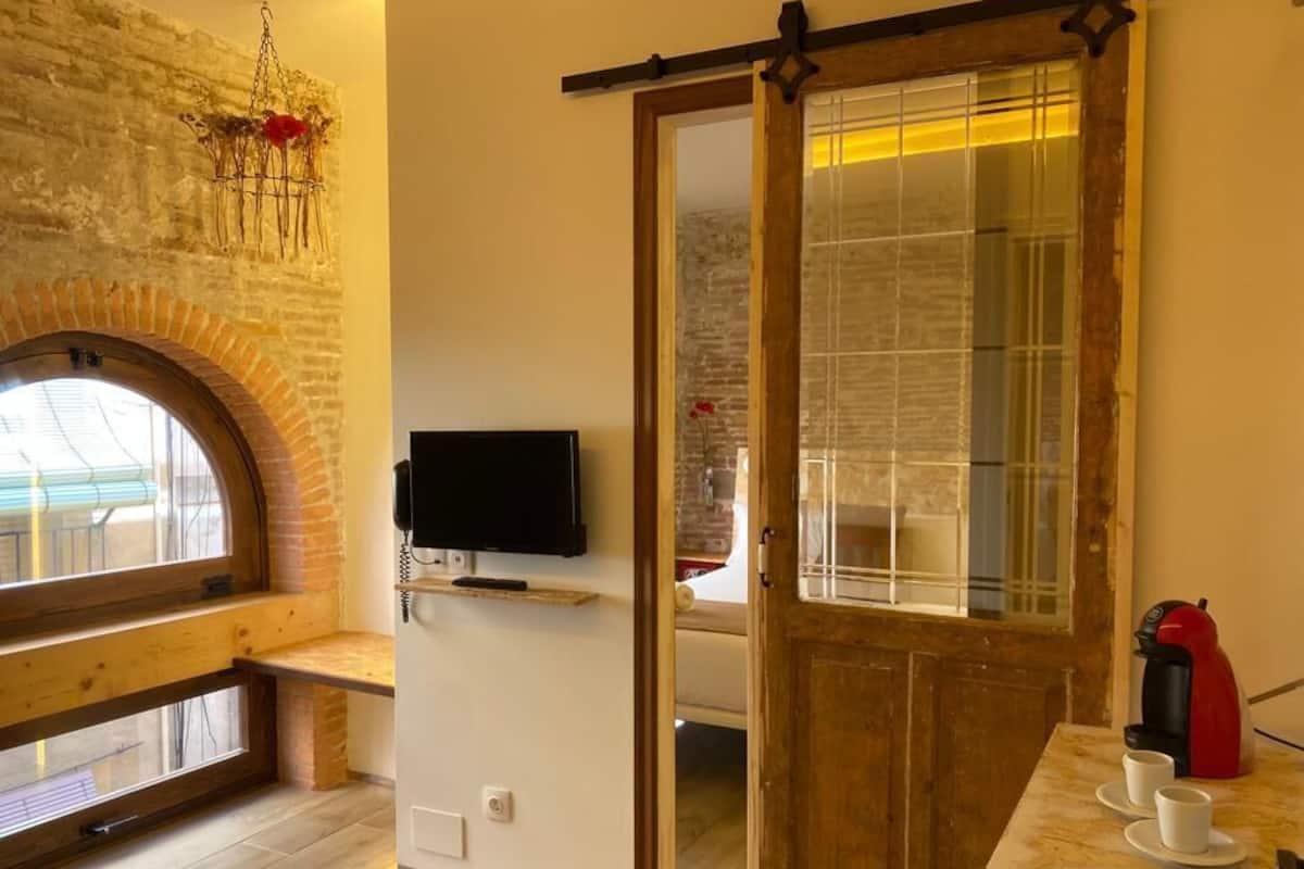 Ein gemütliches Zimmer mit einer hölzernen Bank, einem Fernseher, einer Schiebetür und einer Kaffeestation.