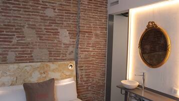 Un baño moderno con pared de ladrillo, un espejo redondo y un lavamanos blanco.