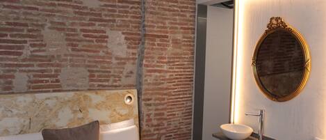 A modern bathroom with a brick wall, a round mirror, and a white sink.