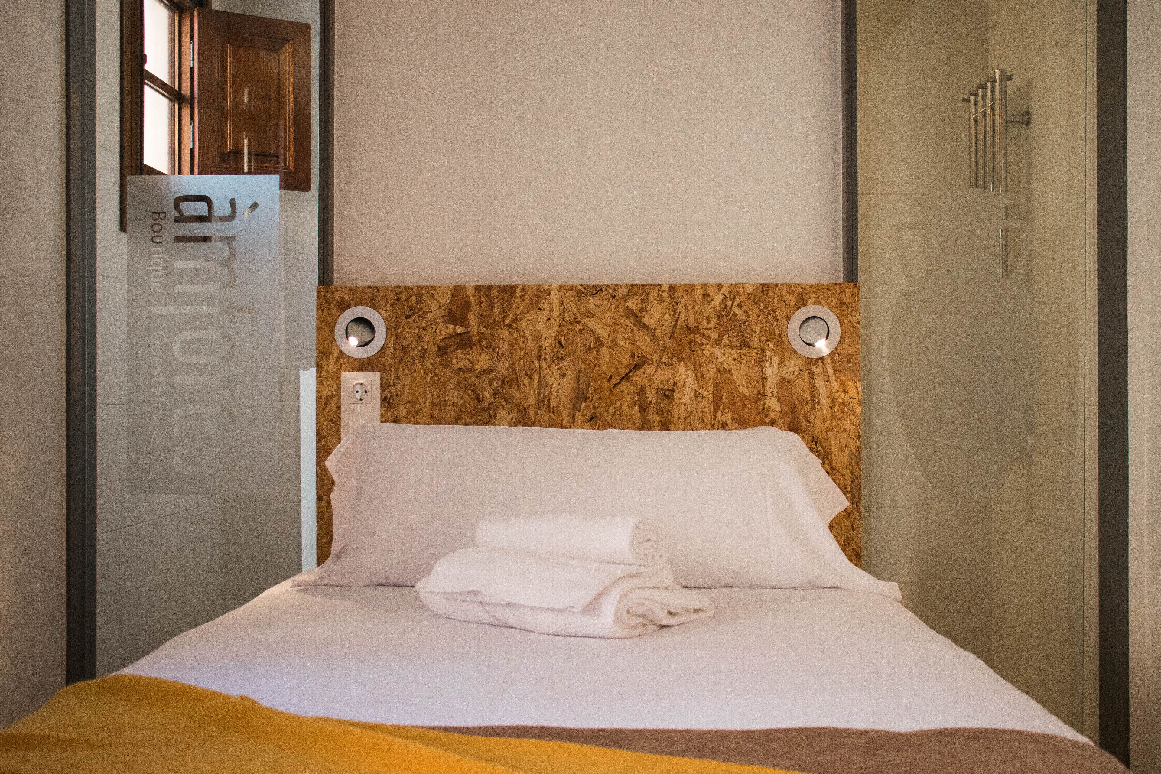 Una habitación de hotel moderna con un cabecero de mármol, una cama con ropa blanca impecable y un box de ducha de vidrio.