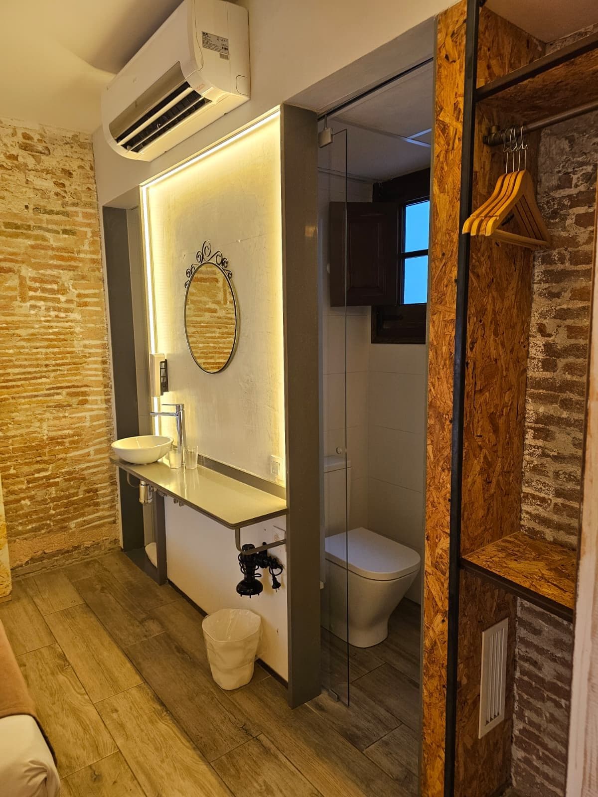 Un baño moderno con tocador de madera, un espejo redondo y cabina de ducha de vidrio.