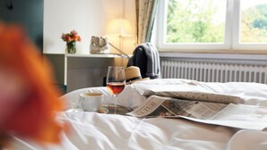 Una cama bien hecha con un periódico, una copa de vino y una taza de café.