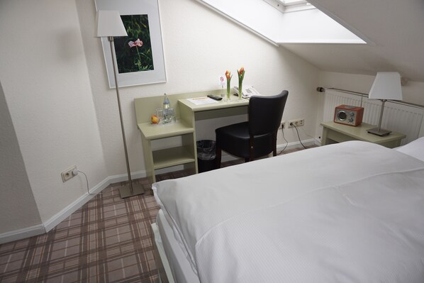 A hotel room with a bed, a desk with a chair, a small table with a lamp, a radiator, and a picture on the wall. - Landgasthof Läuterhäusle (Aalen)