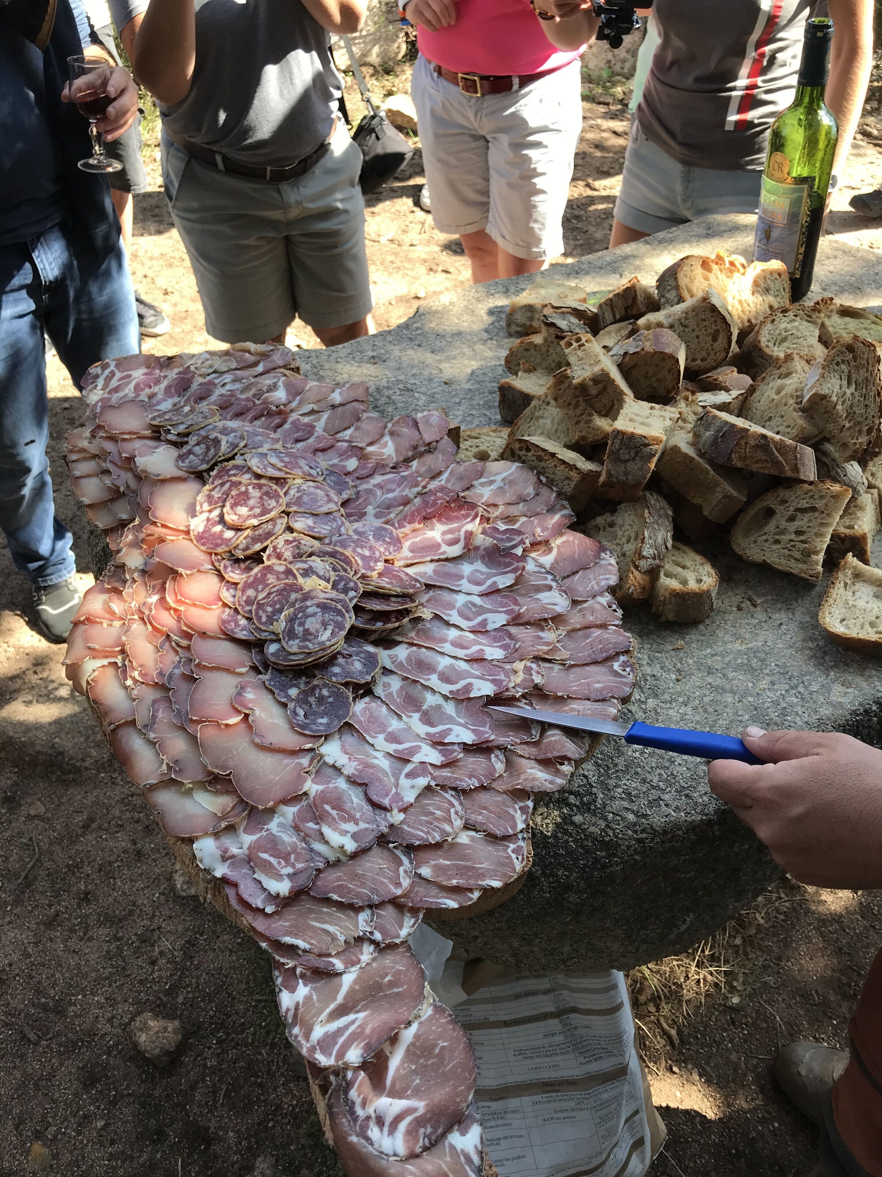 A charcuterie board with various meats and bread, a knife, and a bottle of wine.