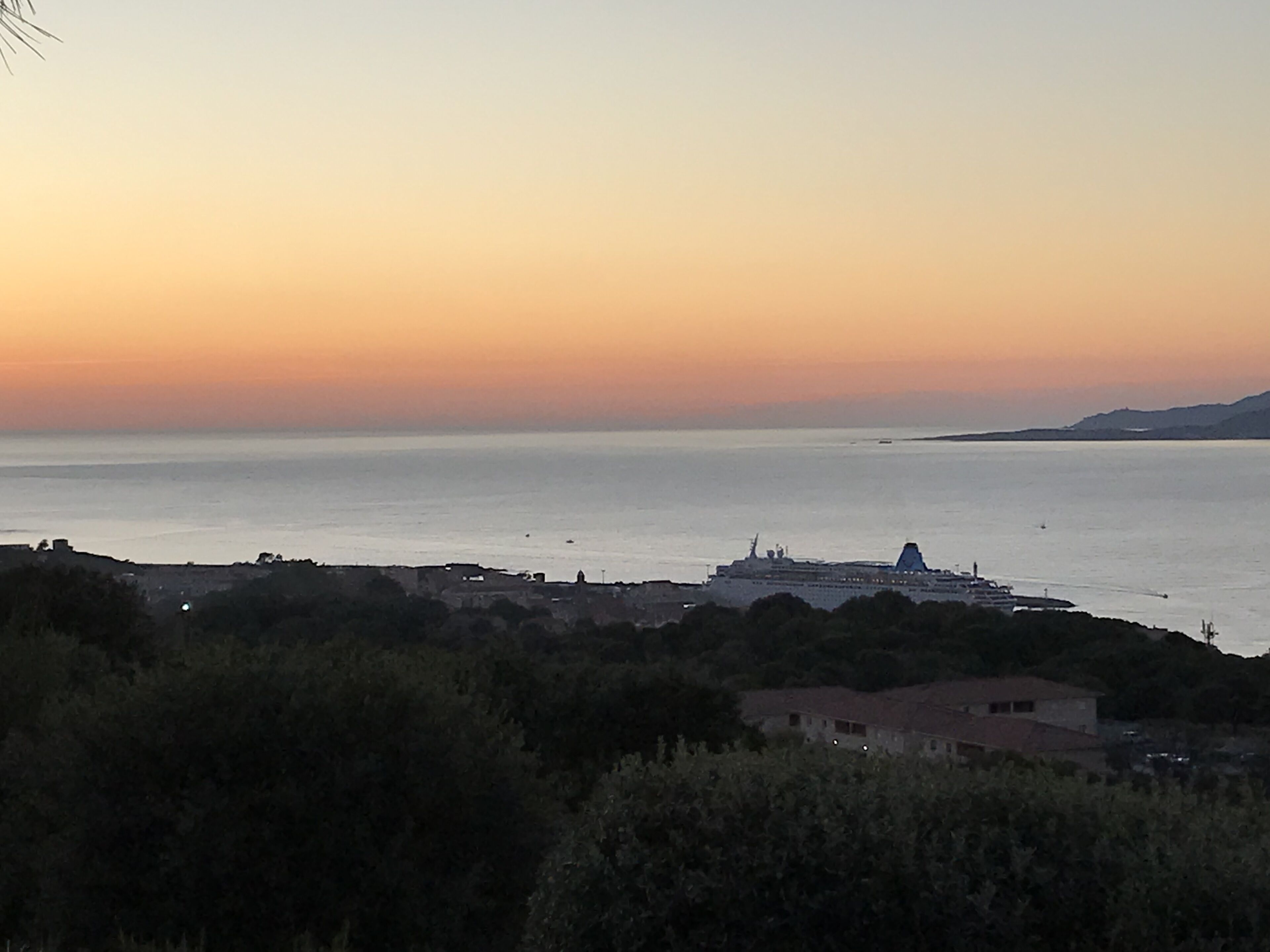 Vista costera con un crucero anclado cerca de un pueblo, rodeado de colinas y vegetación.