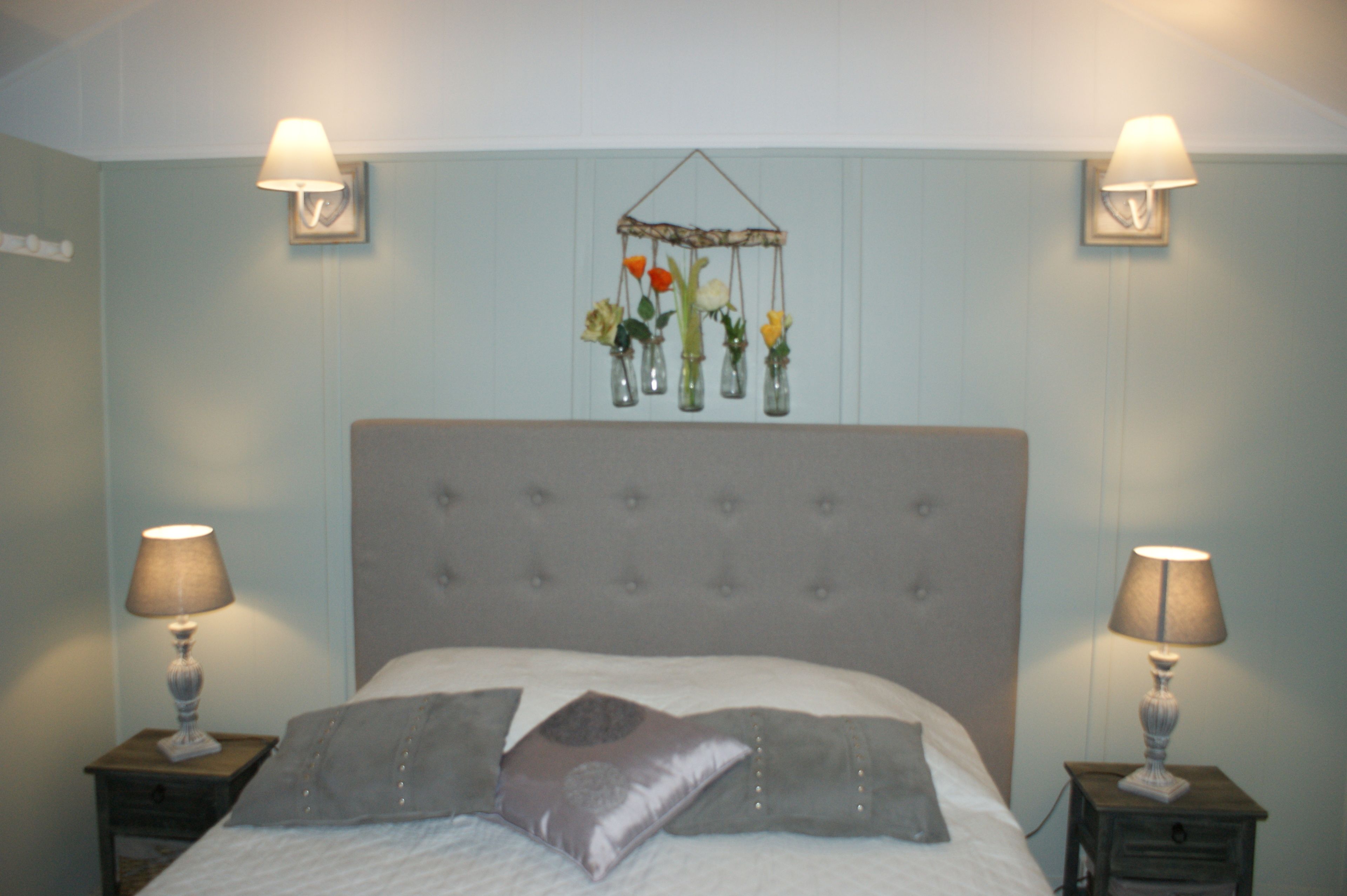 A bedroom with a tufted headboard, a hanging flower arrangement, and two bedside lamps.