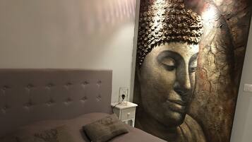 A bedroom with a large Buddha painting on the wall, a tufted headboard, and a bedside table with a lamp.