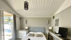 Een slaapkamer met een bed, nachtkastjes, een bureau met een televisie en een deur naar een balkon.
