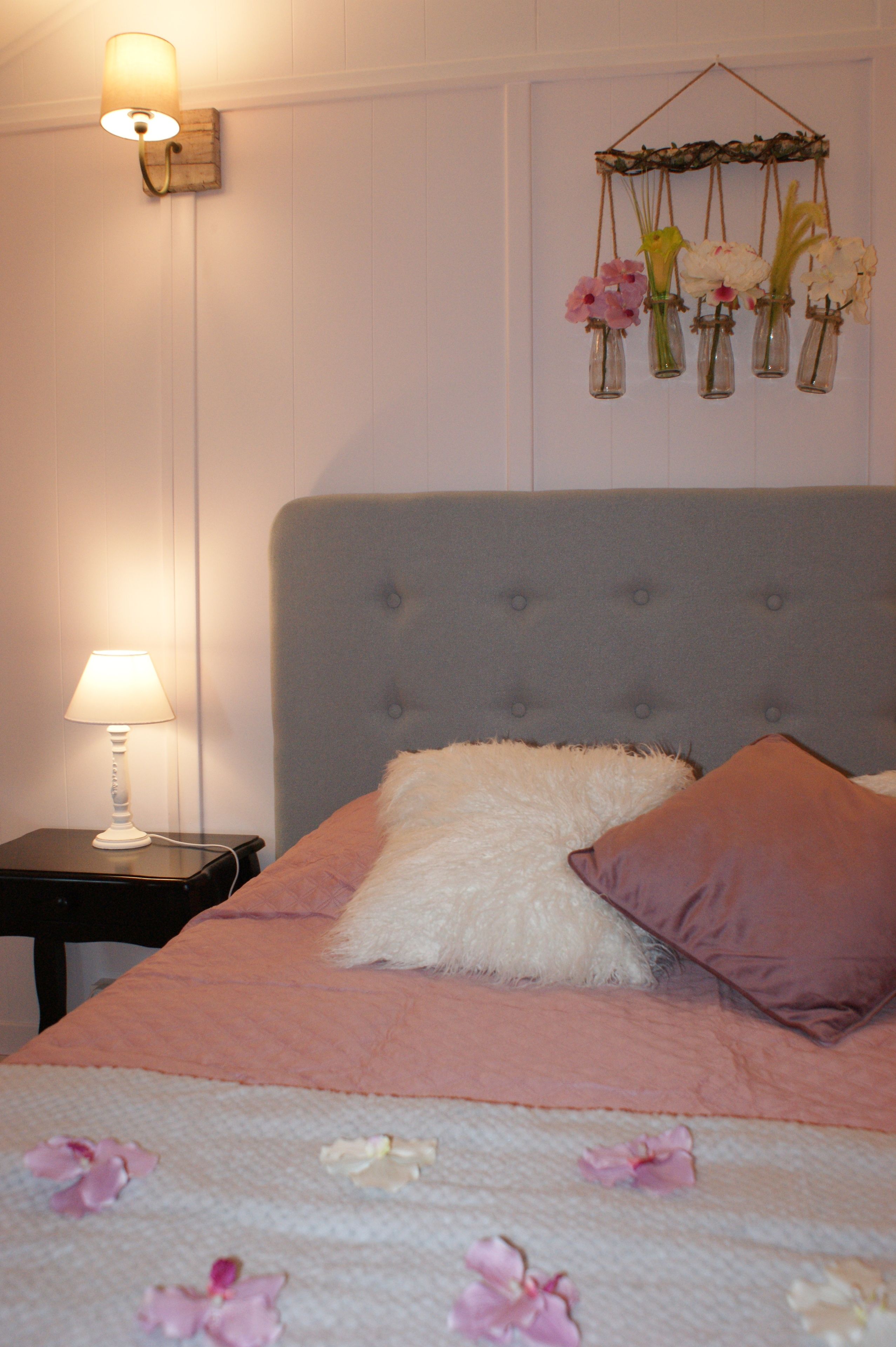 Un dormitorio con cabecera capitonada, mesita de noche con lámpara y un arreglo floral en la pared.