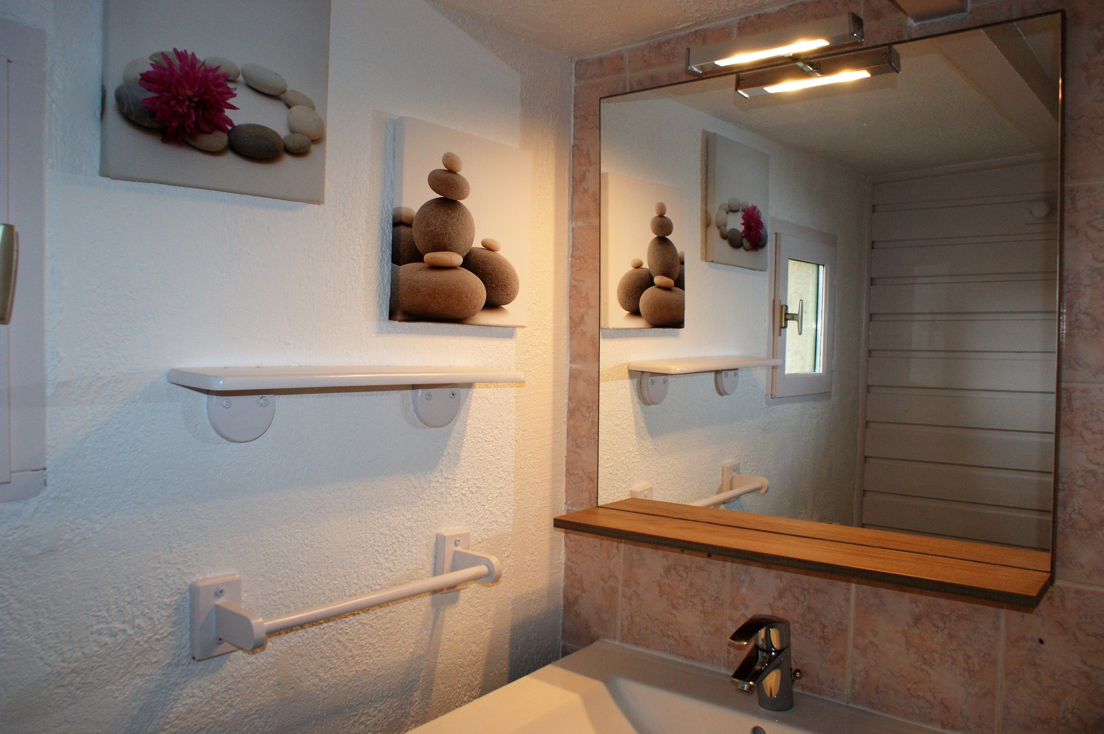 A bathroom with a white sink, a mirror, and shelves with decorative stones and flowers.