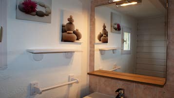 A bathroom with a white sink, a mirror, and shelves with decorative stones and flowers.