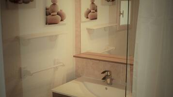 A bathroom with a glass shower enclosure, a sink with a mirror above it, and a towel rack.