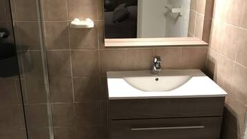 A bathroom with a glass shower enclosure, a sink with a mirror above it, and a small orange trash bin.