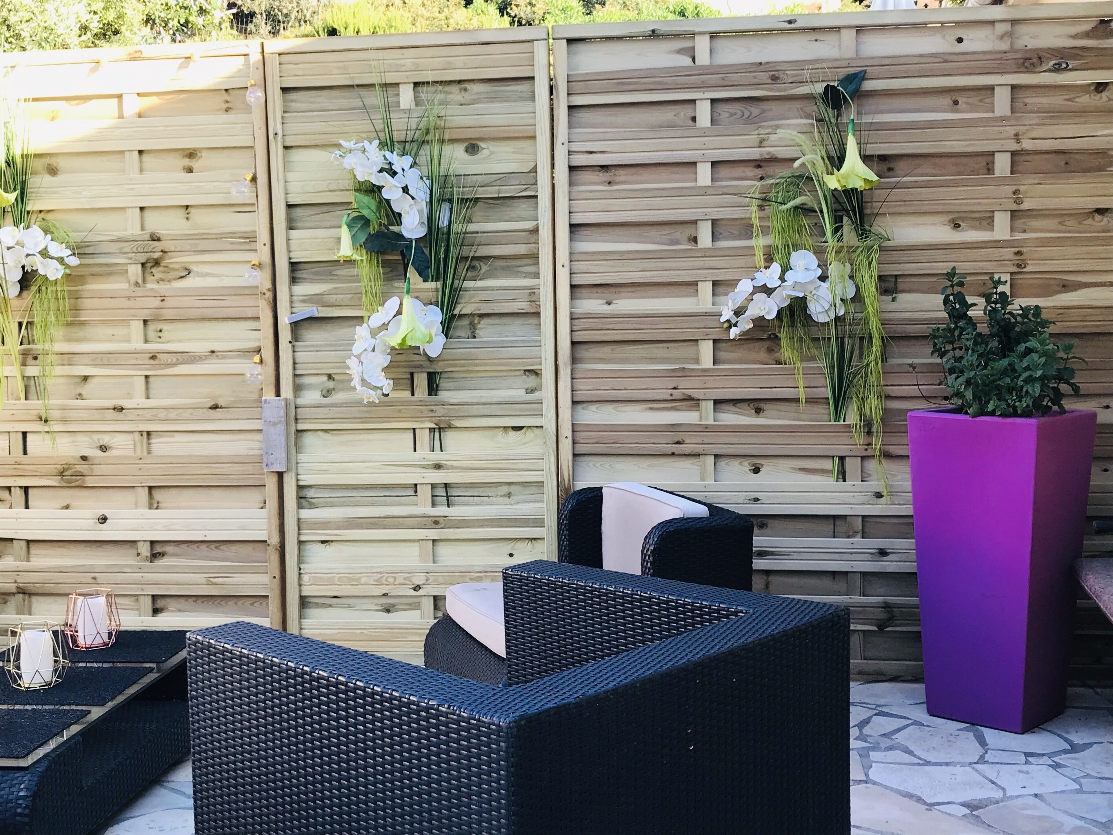 A wooden fence with hanging flower arrangements and a purple planter.