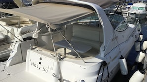 Een witte boot met een zonnescherm, genaamd 'Nosy be', afgemeerd in een jachthaven.