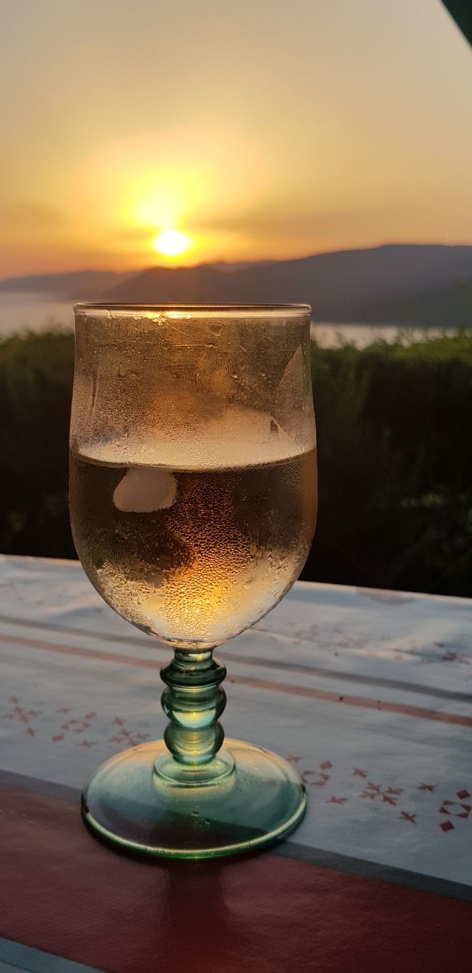 Ett glas med vätska står på ett bord med en solnedgång i bakgrunden.
