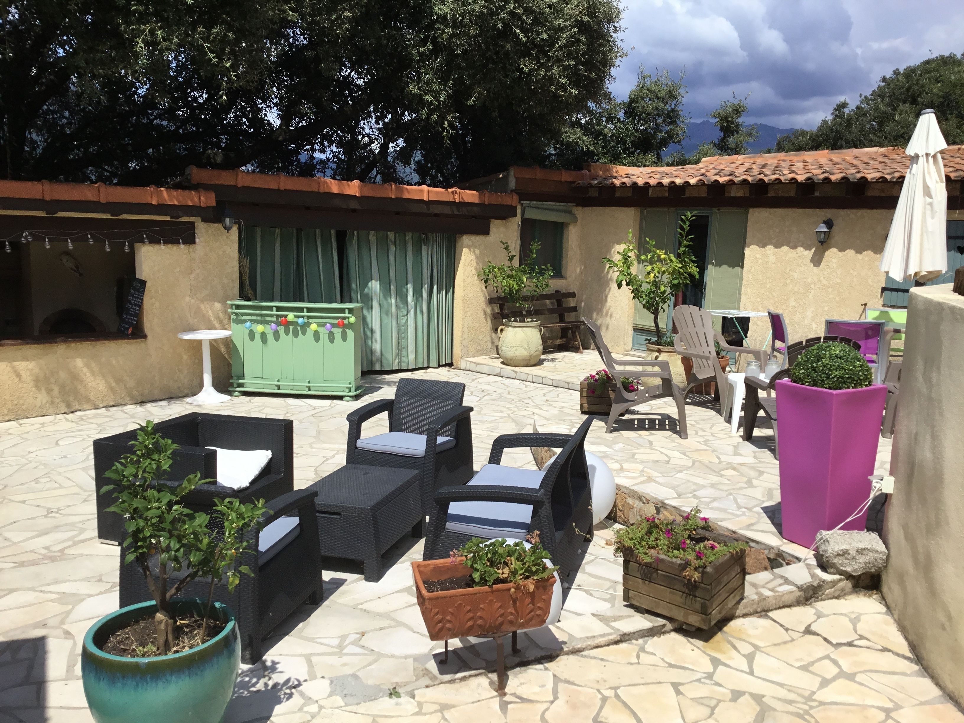 An outdoor patio with stone flooring, wicker furniture, potted plants, and a green cabinet.