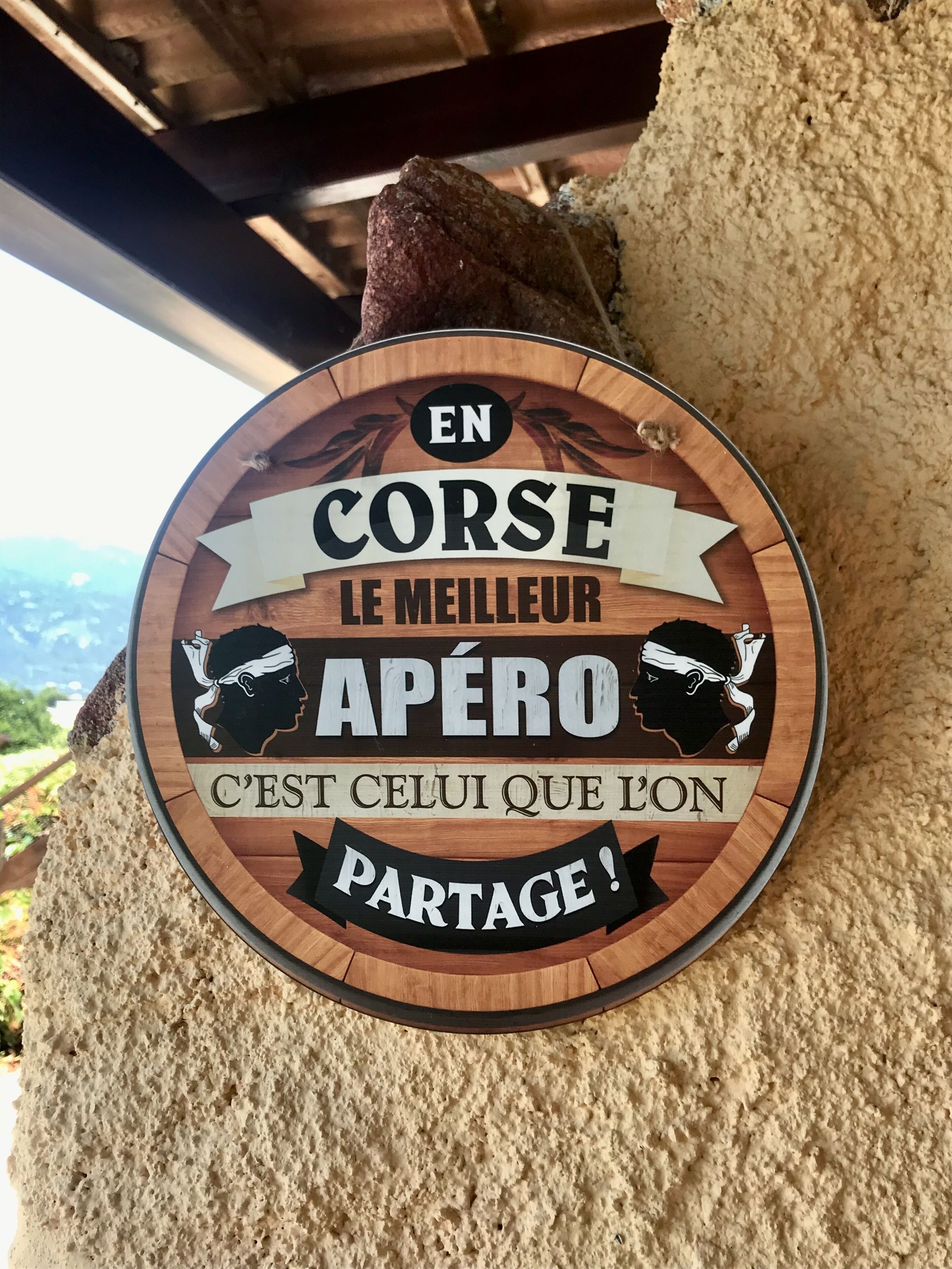 Una señal de madera con texto e ilustración de un perro pequeño, fijada en una pared con textura.