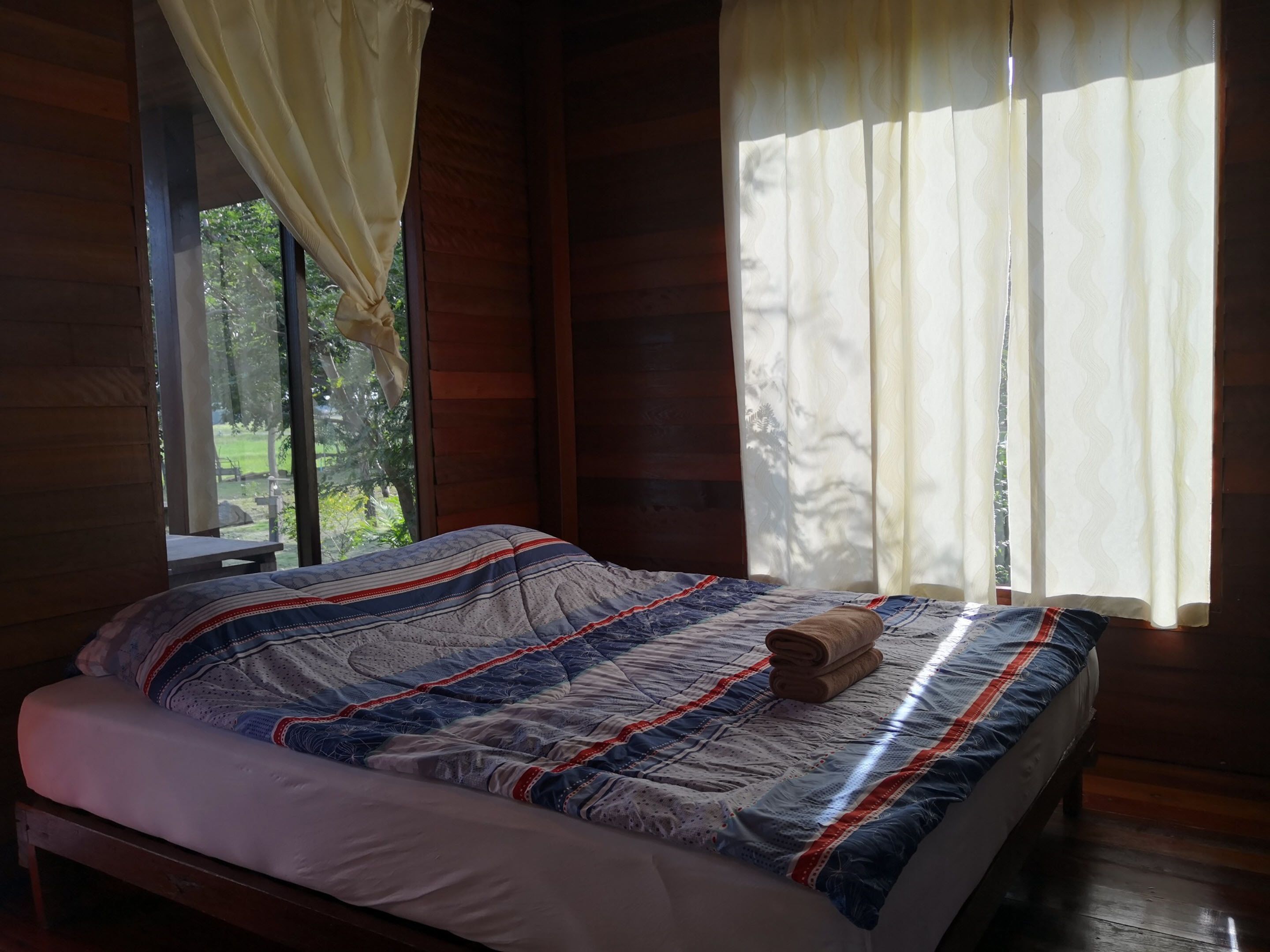 Ein Schlafzimmer einer Holzhütte mit Bett, Vorhängen und Blick auf grüne Landschaft.