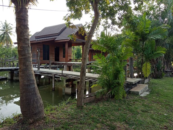 Una casa de madera con techo de tejas, un muelle que se adentra en el agua, y abundante vegetación alrededor.