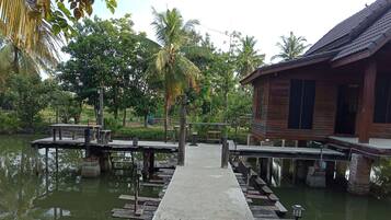 A wooden dock leading to a house by a calm water body, surrounded by lush greenery.