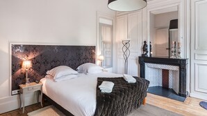 A bedroom with a large bed, bedside lamps, a fireplace, and a mirror. - La Maison du Champlain (Lille)