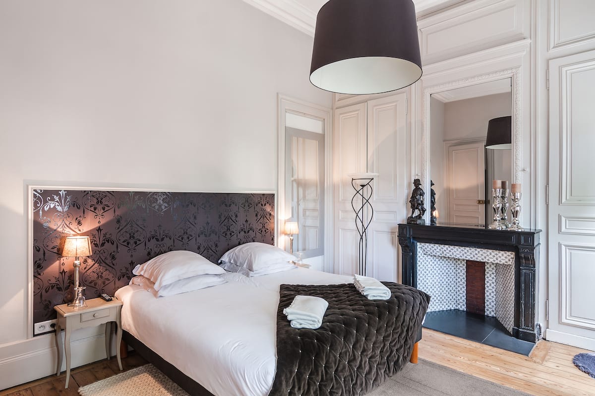 A bedroom with a large bed, bedside lamps, a fireplace, and a mirror.