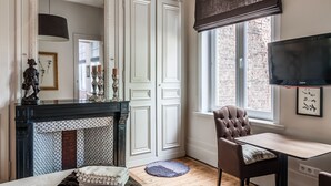 A room with a fireplace, a television, a window with a view of a brick building, and a chair. - La Maison du Champlain (Lille)