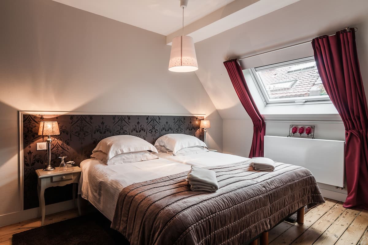 A bedroom with a bed, nightstands, a lamp, a window with curtains, and a skylight.