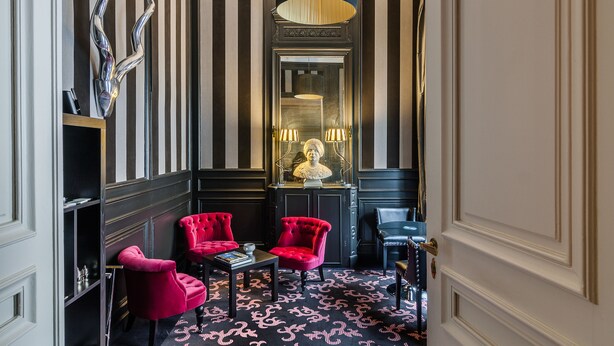 A room with striped walls, a large mirror, two red armchairs, a black table, and a hanging light fixture. - La Maison du Champlain (Lille)