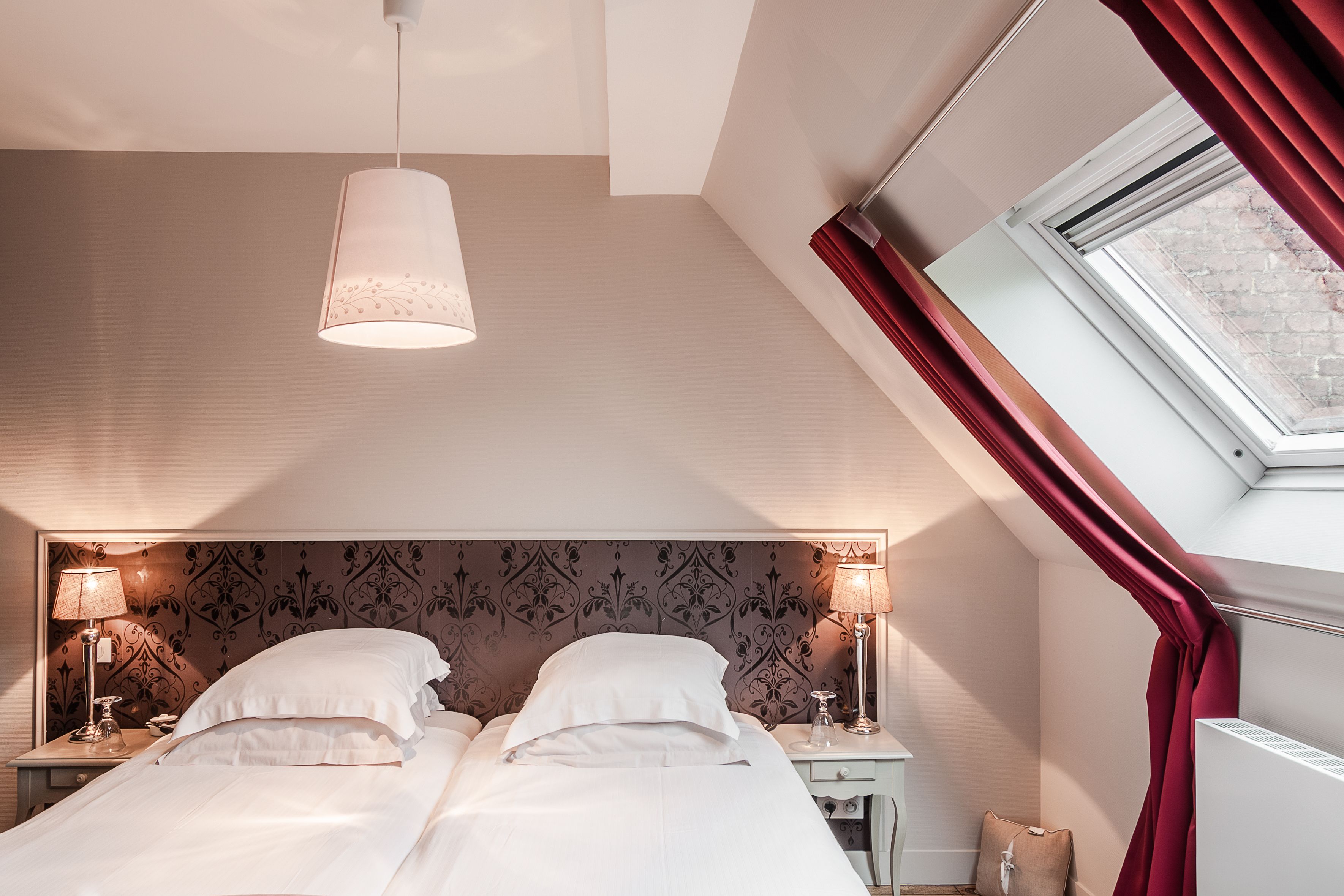 Een slaapkamer met twee bedden, een dakraam en behang met een patroon.