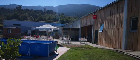 A pool area with lounge chairs and umbrellas, a wooden building with a sign, and a view of a forested hill in the background.