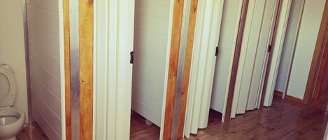 A row of white partitioned stalls with wooden frames, a toilet, and a wooden floor.