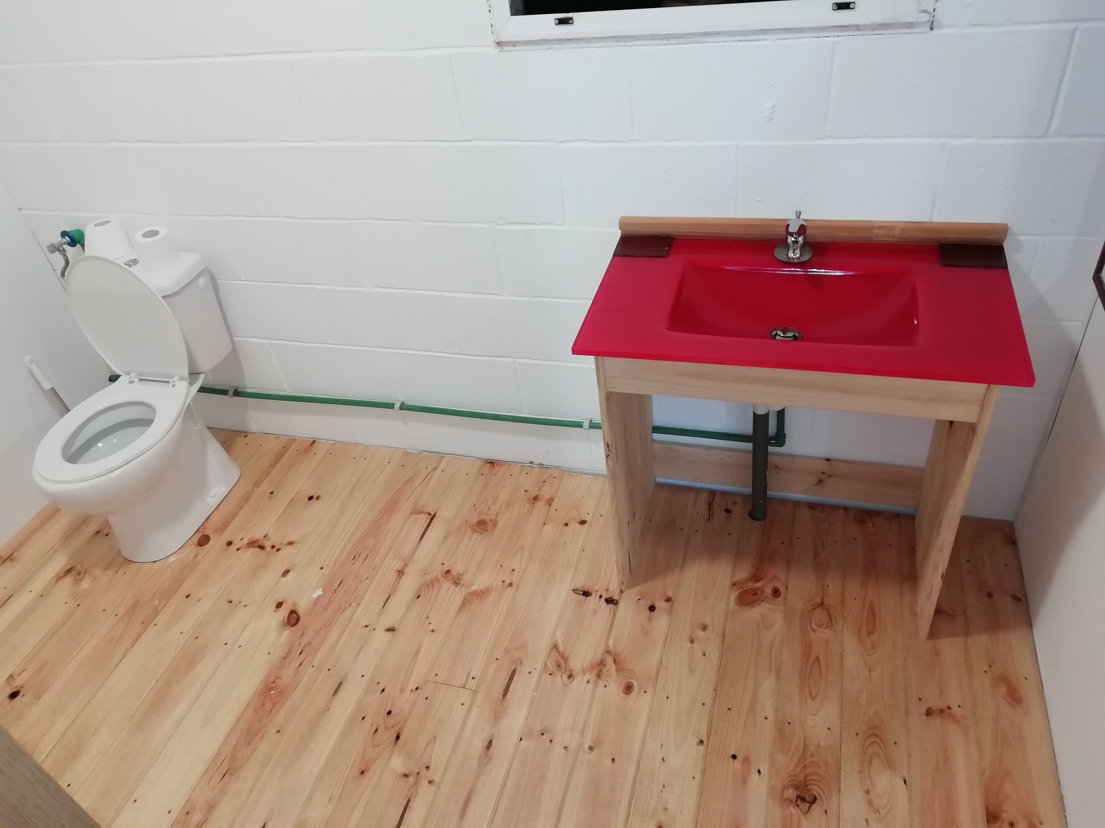 A bathroom with a white toilet, a red sink, and wooden flooring.