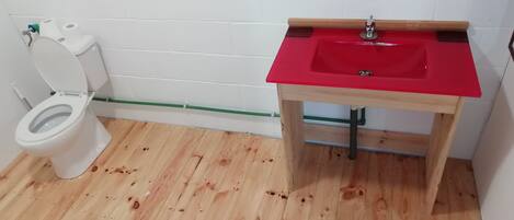 A bathroom with a white toilet, a red sink, and wooden flooring.