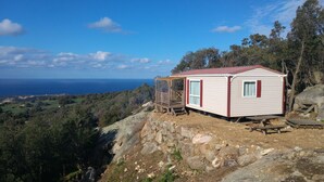 A small cabin with a red roof and white walls, situated on a rocky hillside with a view of the ocean. - Monte Ortu (Lumio)
