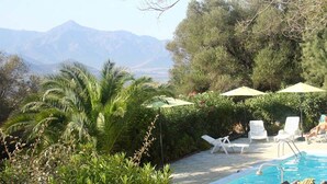 A pool area with lounge chairs and umbrellas, surrounded by greenery and mountains in the background. - Monte Ortu (Lumio)