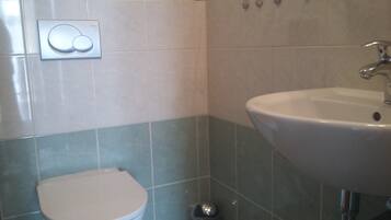 A bathroom with a toilet, a sink, and a wall-mounted flush button.