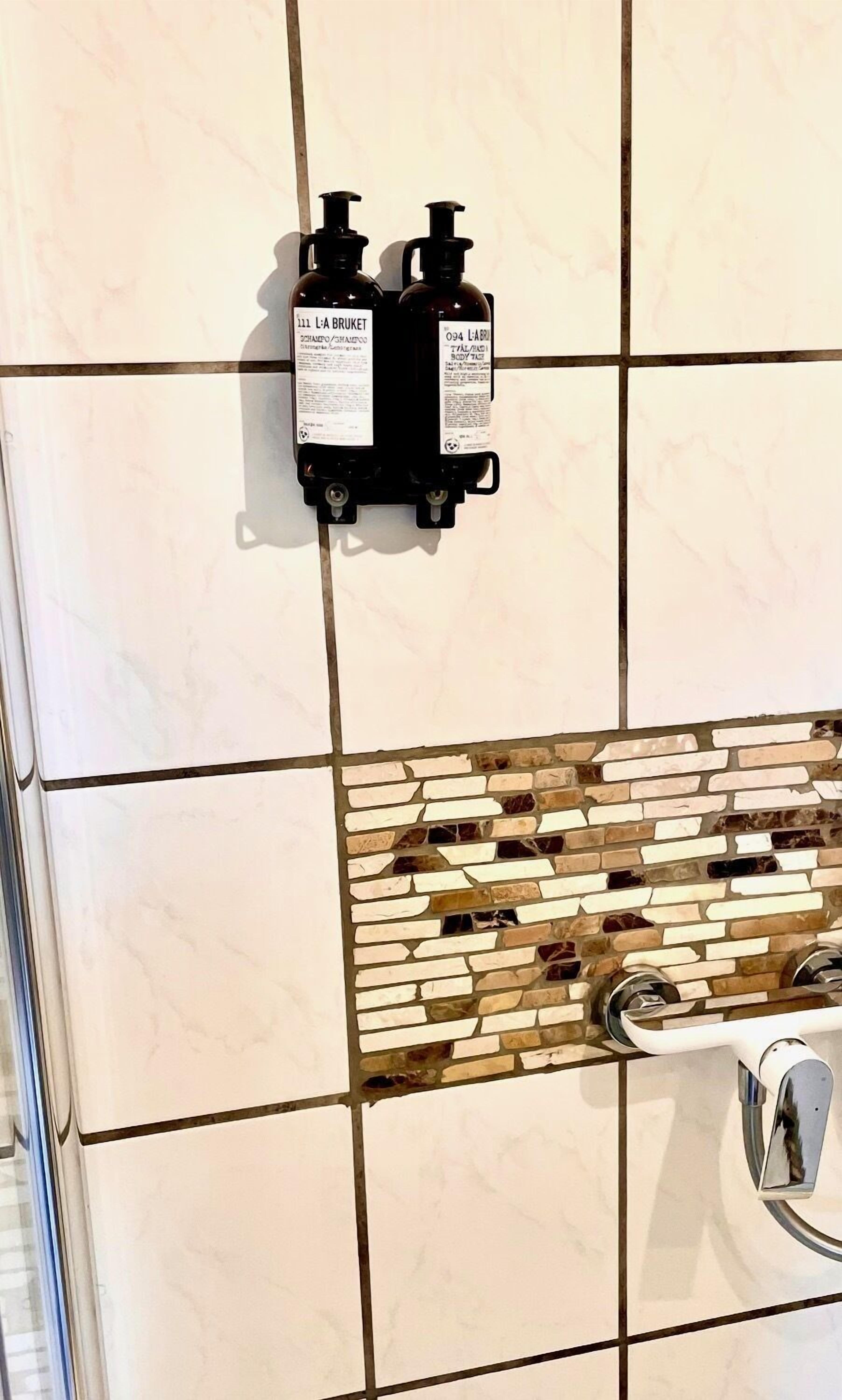 A bathroom with a tiled wall, a soap dispenser, and a shower control panel.