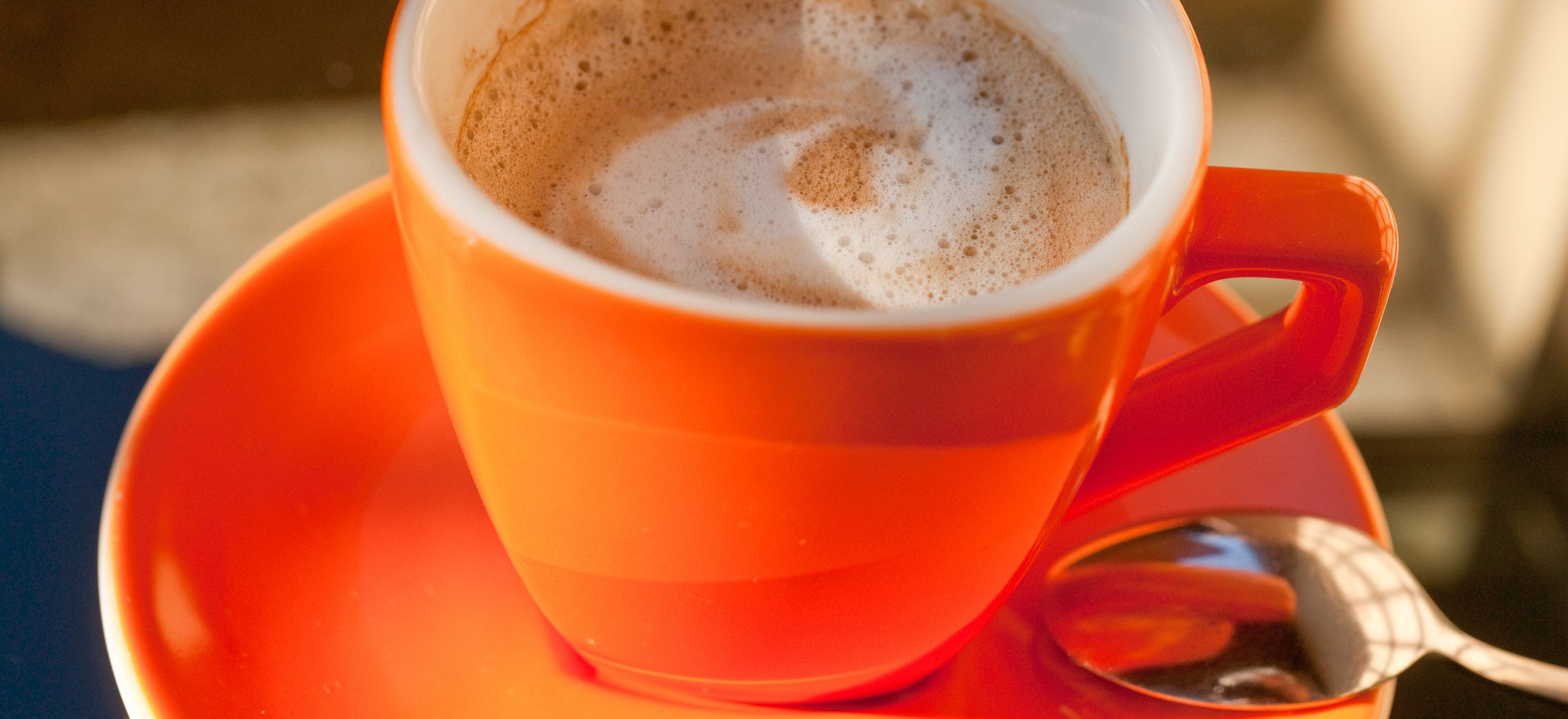 Un gros plan d’une tasse rouge avec une cuillère posée sur une soucoupe.
