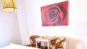 A hotel room with a bed, a table, two chairs, a wall-mounted picture of a rose, and a large red spherical object on the floor. - Hotel Klostermühle (Hann. Muenden)