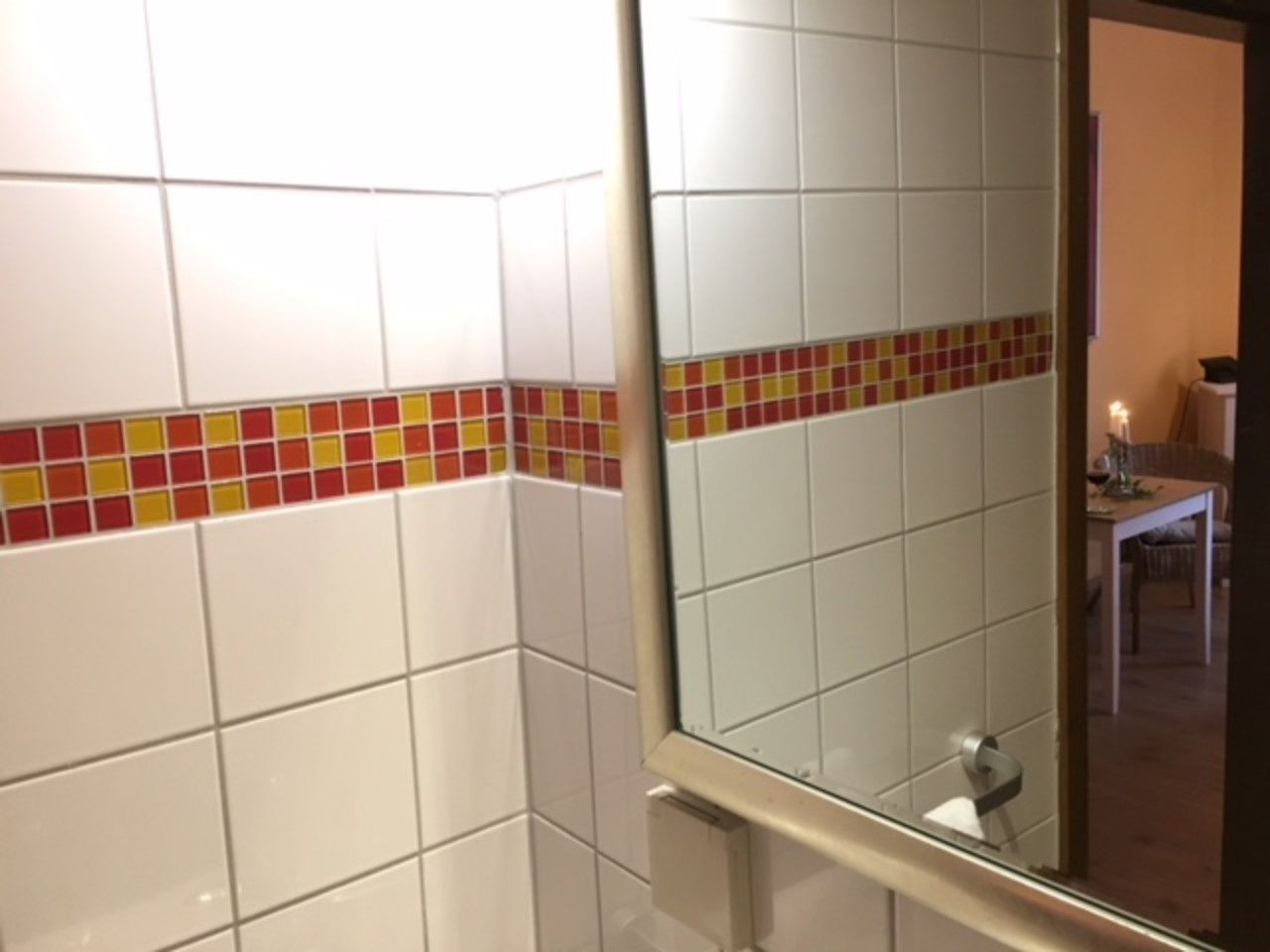 Un baño con baldosas blancas y un borde colorido.