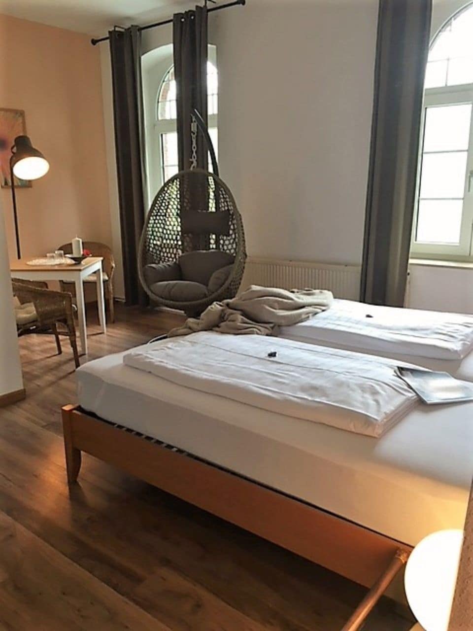 A bedroom with two beds, a hanging chair, a desk, and a lamp.
