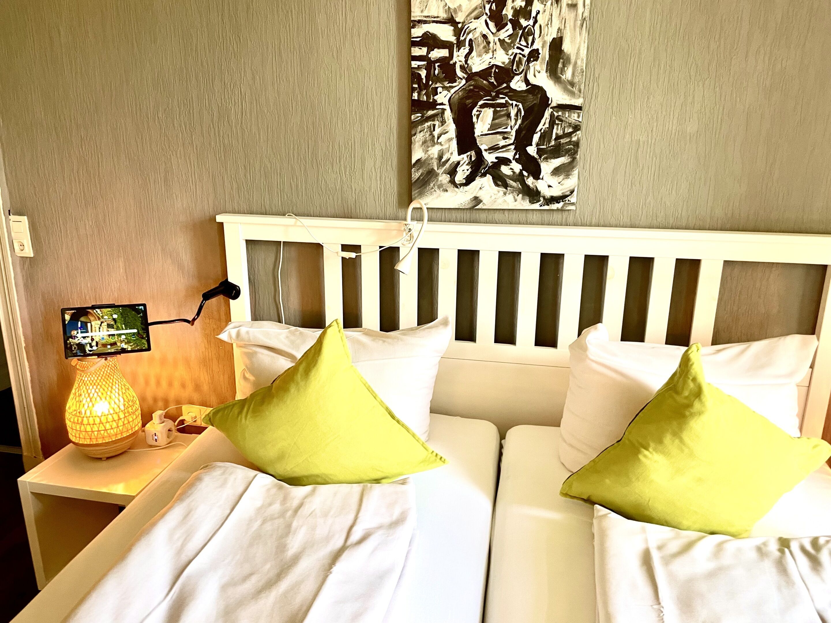 A hotel room with a bed, pillows, a nightstand, a lamp, and a wall art piece.