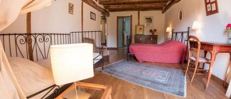 A cozy room with a bed, a desk, and a chair. There is a wooden ceiling and a rug on the floor.