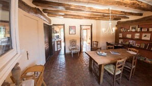 Un comedor rústico con una mesa y sillas de madera, un candelabro y una estantería con fotografías enmarcadas.