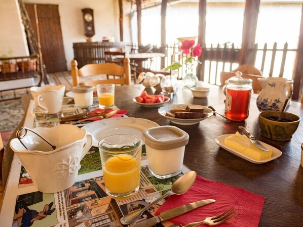 Une table de petit-déjeuner dressée avec divers aliments, notamment une carafe de jus d’orange, un verre de lait, une assiette de toasts et un bol de fraises.