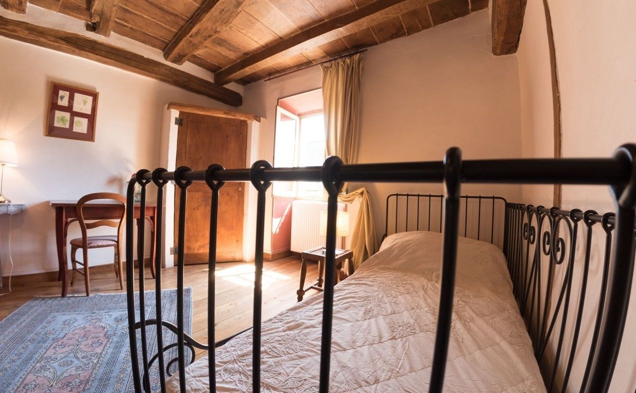 Une chambre à coucher avec un lit en métal, une chaise en bois, une petite table et un tapis à motifs.