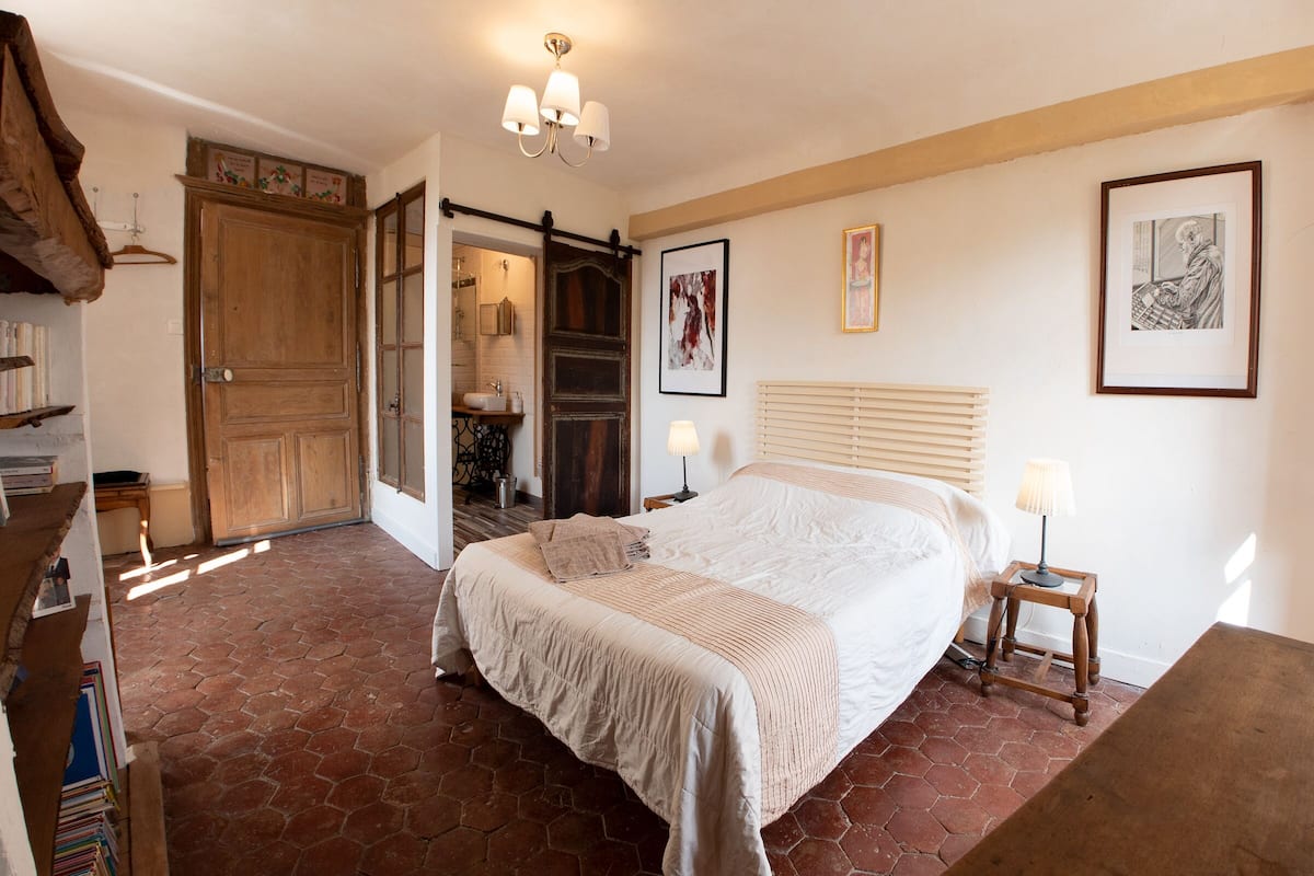 Quarto com uma cama grande, guarda-roupa de madeira, uma mesinha com abajur e uma estante de livros.