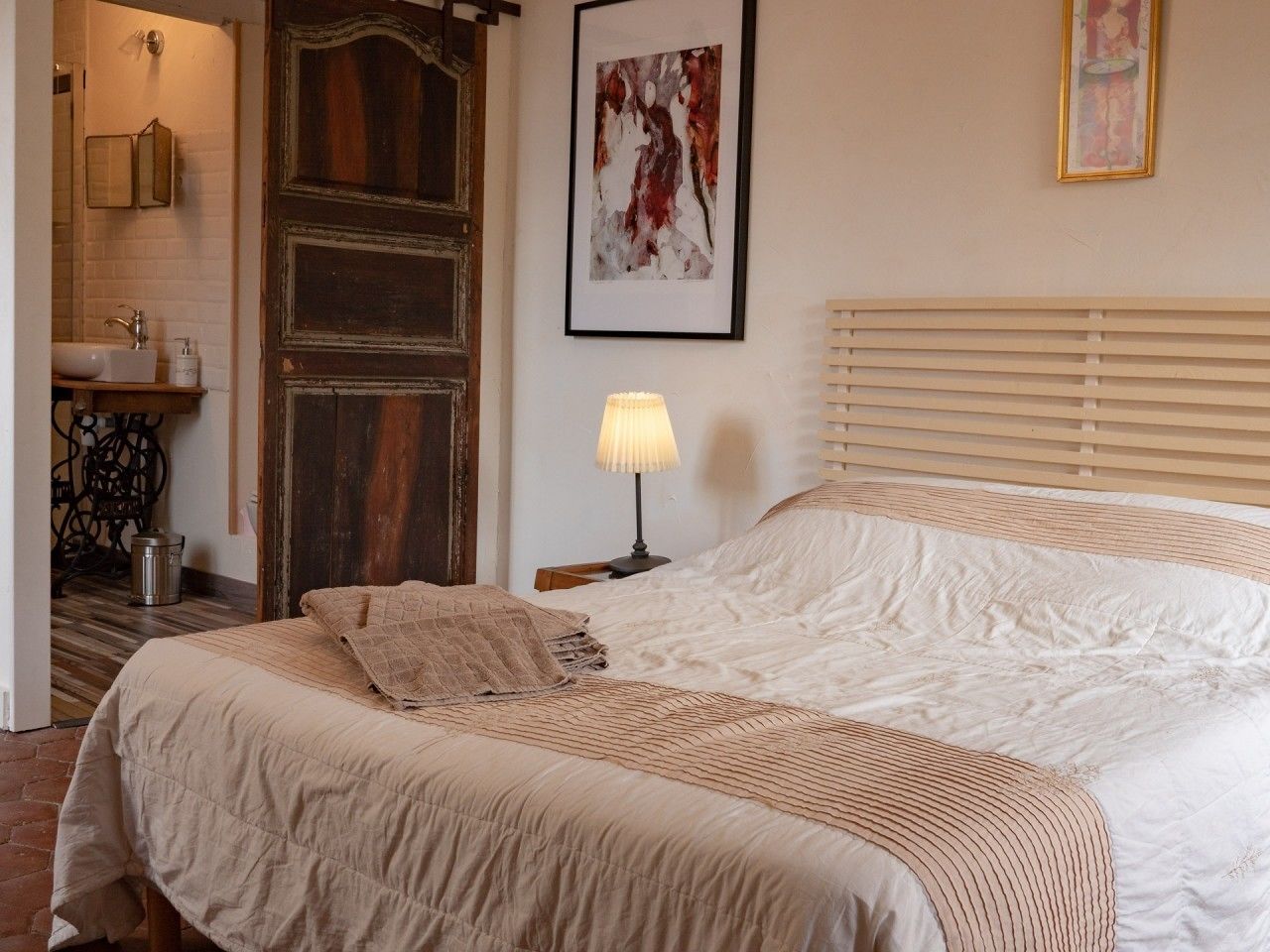 Une chambre à coucher avec un lit, une lampe de chevet, un tableau abstrait encadré et une porte en bois.